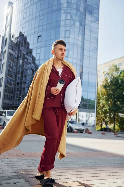 Running, late for the work. Young man in pajama is outdoors on the street. Feels sleepy.