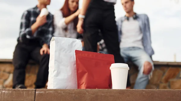 Red package of coffee. Group of young cheerful friends that is outdoors having fun together.