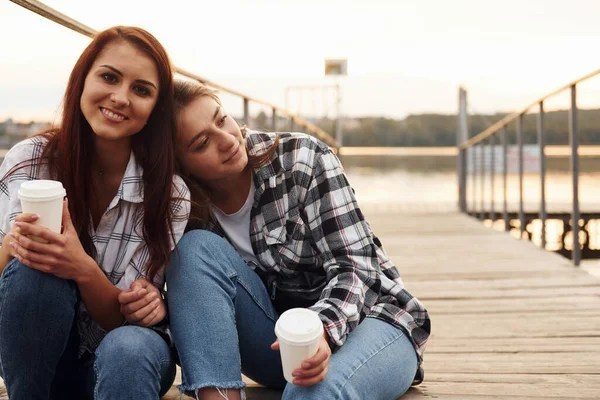 Mignon Lesbienne Couple Assis Ensemble Près Lac Avec Tasses Boisson — Photo