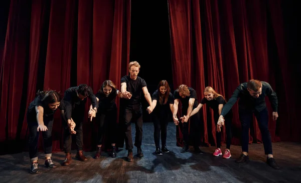 People bowing to audience. Group of actors in dark colored clothes on rehearsal in the theater.