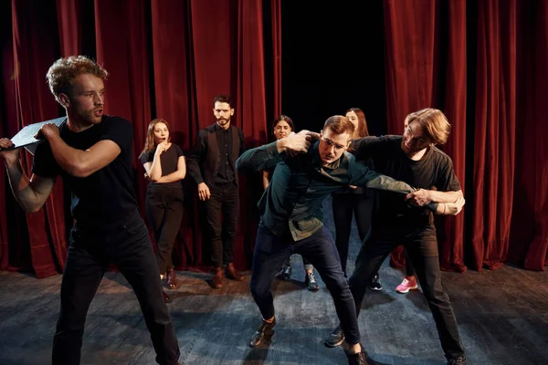 Fight scene. Group of actors in dark colored clothes on rehearsal in the theater.