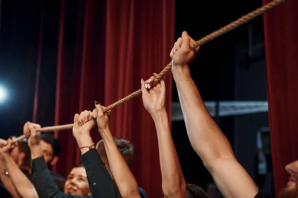 Holding rope in hands above the heads. Group of actors in dark colored clothes on rehearsal in the theater.