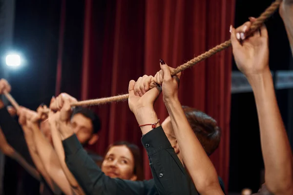 Holding rope in hands above the heads. Group of actors in dark colored clothes on rehearsal in the theater.