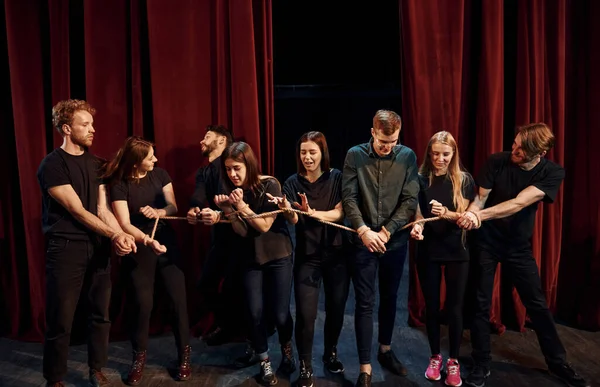 With rope in hands. Group of actors in dark colored clothes on rehearsal in the theater.