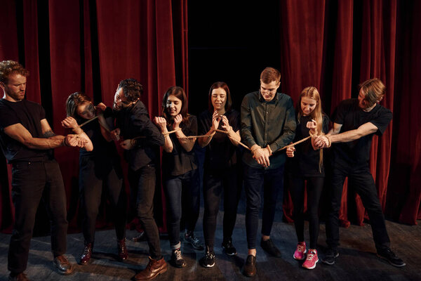 С верёвкой в руках. Группа актёров в тёмной одежде на репетиции в театре.