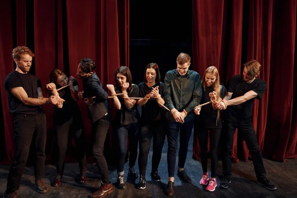 With rope in hands. Group of actors in dark colored clothes on rehearsal in the theater.