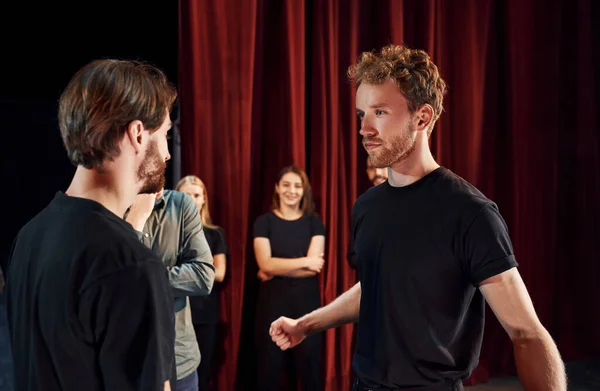 Two people talking. Group of actors in dark colored clothes on rehearsal in the theater.