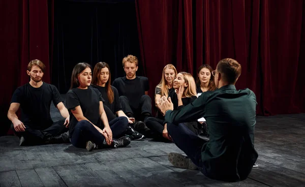 Sitting on the floor. Group of actors in dark colored clothes on rehearsal in the theater.