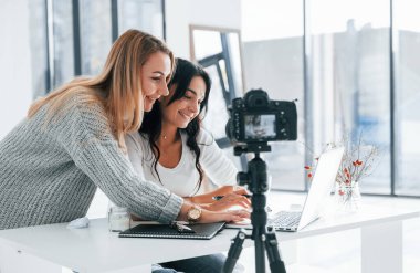 Tripodun üzerindeki kamera kaydediyor. Ofiste dizüstü bilgisayarla çalışan iki serbest çalışan genç bayan..