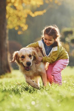 Küçük kız gündüz vakti Golden Retriever köpeğiyle parkta yürüyüşe çıkıyor..