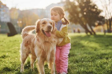 Küçük kız gündüz vakti Golden Retriever köpeğiyle parkta yürüyüşe çıkıyor..