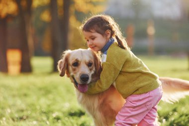 Küçük kız gündüz vakti Golden Retriever köpeğiyle parkta yürüyüşe çıkıyor..