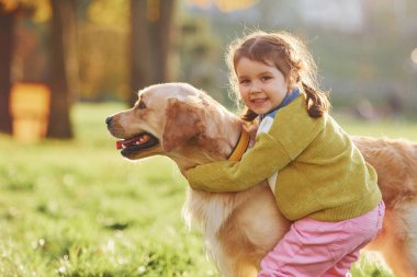 Küçük kız gündüz vakti Golden Retriever köpeğiyle parkta yürüyüşe çıkıyor..