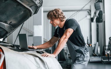 Bilgisayar kullanarak. Gri üniformalı yetişkin adam otomobil salonunda çalışıyor..