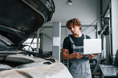 Bilgisayar kullanarak. Gri üniformalı yetişkin adam otomobil salonunda çalışıyor..