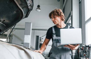 Bilgisayar kullanarak. Gri üniformalı yetişkin adam otomobil salonunda çalışıyor..