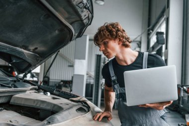 Bilgisayar kullanarak. Gri üniformalı yetişkin adam otomobil salonunda çalışıyor..