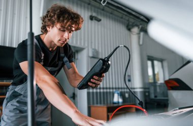 Arabanın elektronik aletlerini test ediyor. Gri üniformalı yetişkin adam otomobil salonunda çalışıyor..