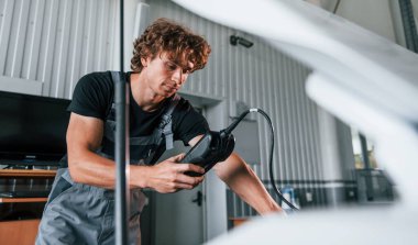 Arabanın elektronik aletlerini test ediyor. Gri üniformalı yetişkin adam otomobil salonunda çalışıyor..