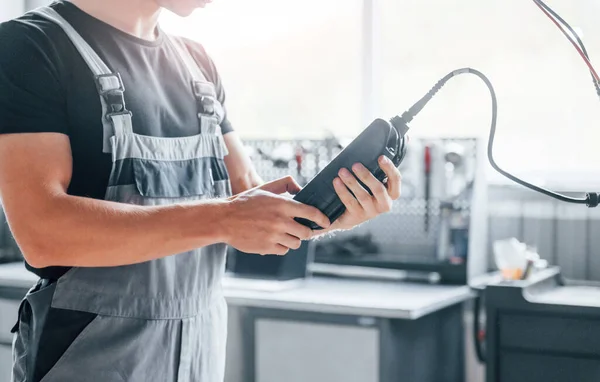 Special tool for testing characteristics. Adult man in grey colored uniform works in the automobile salon.