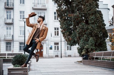 Şapka takıyor ve poz veriyor. Şık giyimli genç erkek manken gündüz vakti şehir dışında..