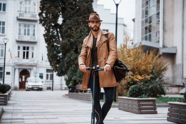 Elektrikli scooter 'da. Şık giyimli genç erkek manken gündüz vakti şehir dışında..