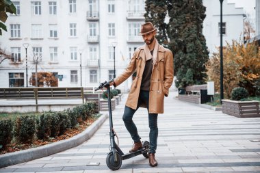 Elektrikli scooter 'da. Şık giyimli genç erkek manken gündüz vakti şehir dışında..
