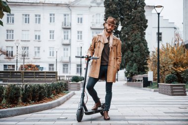 Elektrikli scooter 'da. Şık giyimli genç erkek manken gündüz vakti şehir dışında..