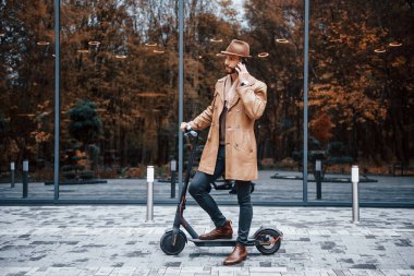 Elektrikli scooter 'da. Şık giyimli genç erkek manken gündüz vakti şehir dışında..