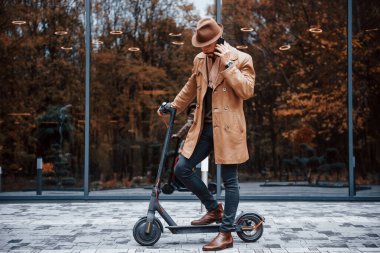 Elektrikli scooter 'da. Şık giyimli genç erkek manken gündüz vakti şehir dışında..