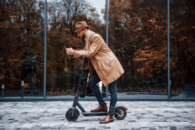 Elektrikli scooter 'da. Şık giyimli genç erkek manken gündüz vakti şehir dışında..