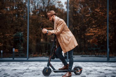 Elektrikli scooter 'da. Şık giyimli genç erkek manken gündüz vakti şehir dışında..