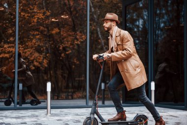 Elektrikli scooter kullanıyorum. Şık giyimli genç erkek manken gündüz vakti şehir dışında..