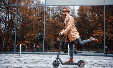Elektrikli scooter kullanıyorum. Şık giyimli genç erkek manken gündüz vakti şehir dışında..