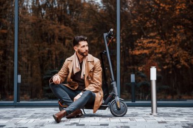 İnşaata ve elektrikli scooter 'a karşı. Şık giyimli genç erkek manken gündüz vakti şehir dışında..