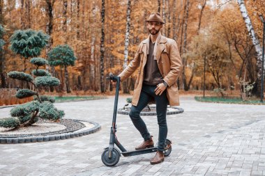 Parkta, elektrikli scooter 'la. Şık giyimli genç erkek model gündüz vakti dışarıda parkta..