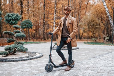 Parkta, elektrikli scooter 'la. Şık giyimli genç erkek model gündüz vakti dışarıda parkta..