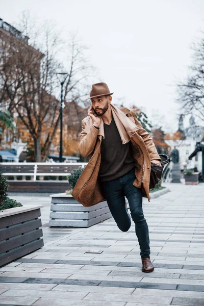 Running, late for meeting. Young male model in fashionable clothes is outdoors in the city at daytime.