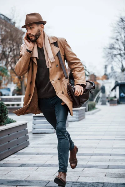 Running, late for meeting. Young male model in fashionable clothes is outdoors in the city at daytime.