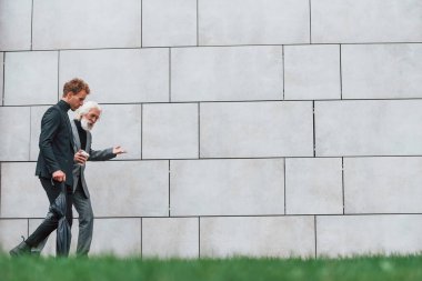 Duvarın yanındaki çimlerde yürüyorum. Zarif giyinmiş son sınıf öğrencisi olan genç adam açık havada birlikte. İş kavramı.