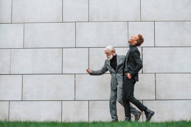 Duvarın yanındaki çimlerde yürüyorum. Zarif giyinmiş son sınıf öğrencisi olan genç adam açık havada birlikte. İş kavramı.