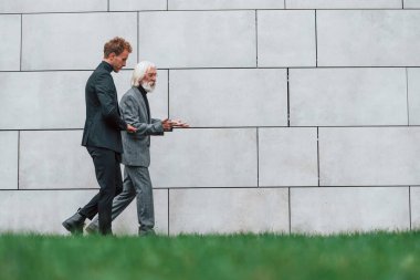 Duvarın yanındaki çimlerde yürüyorum. Zarif giyinmiş son sınıf öğrencisi olan genç adam açık havada birlikte. İş kavramı.