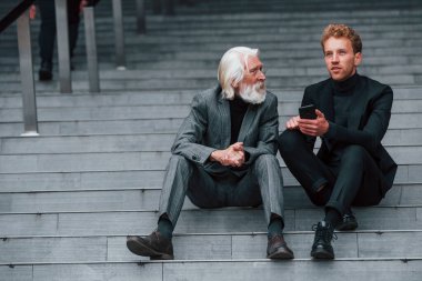 Telefonla oturuyor. Zarif giyinmiş son sınıf öğrencisi olan genç adam açık havada birlikte. İş kavramı.