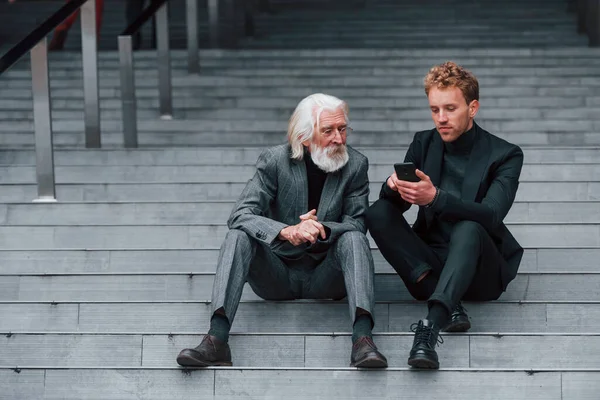 Sentado Com Telefone Jovem Com Homem Sênior Roupas Elegantes Livre — Fotografia de Stock