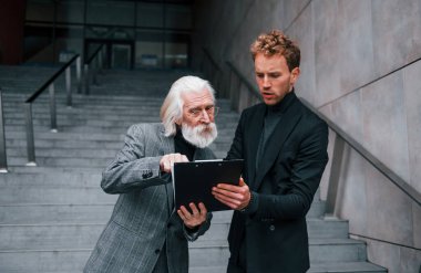 Not defterini tutuyorum. Zarif giyinmiş son sınıf öğrencisi olan genç adam açık havada birlikte. İş kavramı.