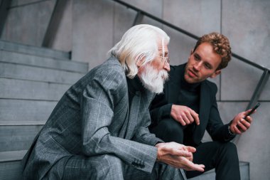 Telefonla oturuyor. Zarif giyinmiş son sınıf öğrencisi olan genç adam açık havada birlikte. İş kavramı.