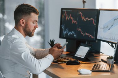 Resmi giyinmiş genç işadamı birden fazla ekranla ofiste..