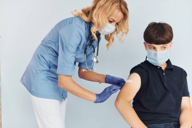 Üniformalı doktor siyah gömlekli çocuğa aşı yapıyor..