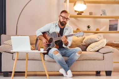 Sıcak bir atmosfer. Gündelik giysiler içinde ve akustik gitarlı bir adam içeride..