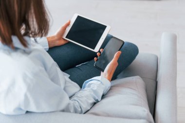 Akıllı telefon ve tablet tutuyor. Genç kadın, gündüz vakti modern evin içinde..